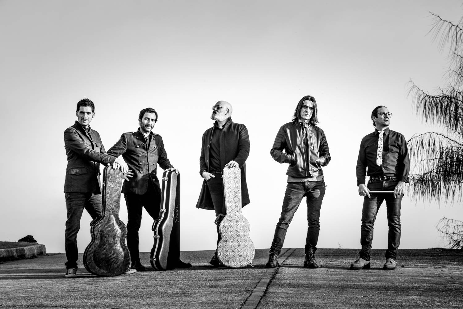 Fotografía en blanco y negro de los miembros de la banda Heiser que aparecen de pie en una carretera junto con algunos de sus instrumentos